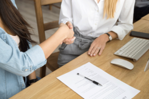 Duas pessoas apertando as mãos sobre uma mesa com um contrato e uma caneta